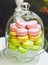 Sweet and colourful french macaroons or macaron in a glass bell jar or glass tray on a white wooden table. Dessert. Can be used fo