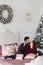 Sweet couple hugging each other on the bed in bedroom decorated for Christmas. Handsome man and pretty model girl in