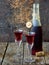 Sweet cranberry alcohol drink liqueur in two glasses and bottle on wooden background.
