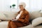 a sweet, enthusiastic elderly lady with gray hair is sitting on the couch working remotely on a laptop and smiling with