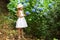 Sweet girl in a hat and white dress walks in the botanical garden on a summer day