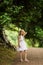 Sweet girl in a hat and white dress walks in the botanical garden on a summer day