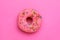 Sweet glazed donut decorated with sprinkles on pink background, top view. Tasty confectionery