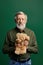 Sweet handsome senior gentleman holding a teddy bear isolated on green background