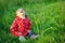 Sweet happy little girl sitting in grass outdoor. Cute baby with curly hair laughting. Young girl posing in park. Smiling kid.