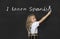 Sweet junior schoolgirl standing happy writing in blackboard I learn Spanish