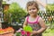 Sweet little girl with curly hair smiles while watering colorful flowers in the garden