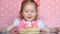 A sweet little girl make a wish and blows out candles on birthday cake at party. Cute child. The concept of a children`s
