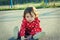 Sweet little girl sitting on the ground outdoor. Cute baby with curly hair looking at camera.