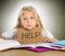 Sweet little school girl holding help sign in stress with books