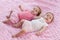 Sweet little twins lying on a pink blanket.