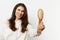 a sweet, pleasant, beautiful woman with well-groomed hair, standing on a light background holding a comb in her hands