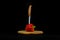 Sweet red pepper with sharp knife is stuck, wooden board and black background