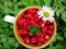 Sweet ripe red wild strawberries in a cup with five leaves clover and daisy flower on a green grass