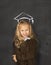 Sweet schoolgirl on blackboard with with chalk sketch drawing of graduation hat smiling happy