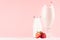Sweet strawberry milkshake in exquisite wineglass with milk bottle, slices berry, straw on light pastel pink background.