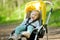 Sweet toddler boy sitting in a stroller outdoors. Little child in pram. Infant kid in pushchair. Summer walks with kids