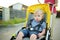 Sweet toddler boy sitting in a stroller outdoors. Little child in pram. Infant kid in pushchair. Summer walks with kids