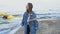 Sweet woman smiling and posing, looking at horizon, standing on shore of disturbing blue sea on cool summer day.