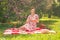 Sweetheart charming pinup girl in a summer dress on a checkered blanket in the Park near the bushes of lilac enjoys life and leisu