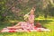 Sweetheart charming pinup girl in a summer dress on a checkered blanket in the Park near the bushes of lilac enjoys life and leisu