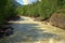 A swift mountain river carries its turbulent waters in a rocky channel through a summer forest on a sunny day