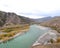 A swift, turbulent turquoise river flows through an autumn valley surrounded by mountain peaks