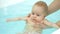 Swim teacher holds baby under arms girl swings legs in bathtub