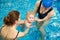 Swimmer baby looking in camera while immersing in water at swimming classes in paddling pool. Teaching swimming, diving