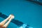 The swimmer`s foot is plunged into a water pool with blue transparent clear water, on which bright sunlight shines. indoor sports