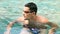 Swimmer. Young athletic brunette man wearing swimming goggles in pool. Panorama banner. Healthy lifestyle. Serious