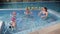 A swimming coach teaches a group of children to swim and dive in an indoor pool.