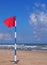 Swimming is dangerous in ocean waves. Red warning flag flapping in the wind on beach at stormy weather