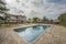 Swimming pool with cleaning hose of a single-family home with stone floors, garden with grass and trees