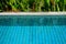 Swimming pool clear water showing turquoise blue clay square tiles and grey cement grout lines with sandwash edge