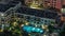 Swimming pool and low rise illuminated buildings in Greens district aerial night timelapse.