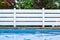Swimming pool side empty relaxation space without people outside garden place water and white deck fence and unfocused trees