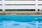 Swimming pool side soft focus blue water surface foreground and white wooden deck garden fence background resort hotel relaxation