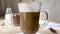 Swirls of milk mixed with dark coffee in cup. Cappuccino or latte in tall glass with handle. Two-layer drink with froth milk.
