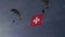 Swiss flag in blue sky flown by military paratrooper. Famous white cross on red