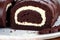 A swiss roll on a white plate on a wooden table. Homemade chocolate roll. Red velvet cake. Generative AI