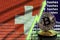 Switzerland flag and rising green arrow on bitcoin mining screen and two physical golden bitcoins