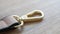 Swivel snap fastener with leather beige bag strap on a wooden background. Metal carabiner with swivel clip or hook. Small gold