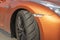 A swivel wheel under the orange fender of a sports car.