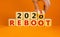 Symbol of 2021 reboot. Businessman turns a wooden cube and changes words `reboot 2020` to `reboot 2021`. Beautiful orange