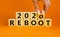 Symbol of 2021 reboot. Businessman turns a wooden cube and changes words `reboot 2020` to `reboot 2021`. Beautiful orange