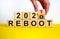 Symbol of 2021 reboot. Businessman turns a wooden cube and changes words `reboot 2020` to `reboot 2021`. Beautiful yellow and