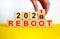 Symbol of 2021 reboot. Businessman turns a wooden cube and changes words `reboot 2020` to `reboot 2021`. Beautiful yellow and
