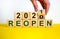 Symbol of 2021 reopen. Businessman turns a wooden cube and changes words `reopen 2020` to `reopen 2021`. Beautiful yellow and