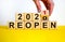 Symbol of 2021 reopen. Businessman turns a wooden cube and changes words `reopen 2020` to `reopen 2021`. Beautiful yellow and